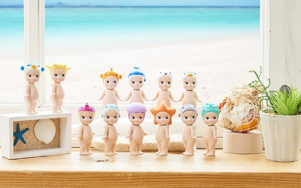 Set of small figurines with colorful hair on a wooden surface with a beach-themed background.